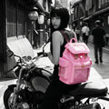 Woman with a pastel pink Cyberpunk Ita Backpack sitting on a motorcycle in an urban setting.
